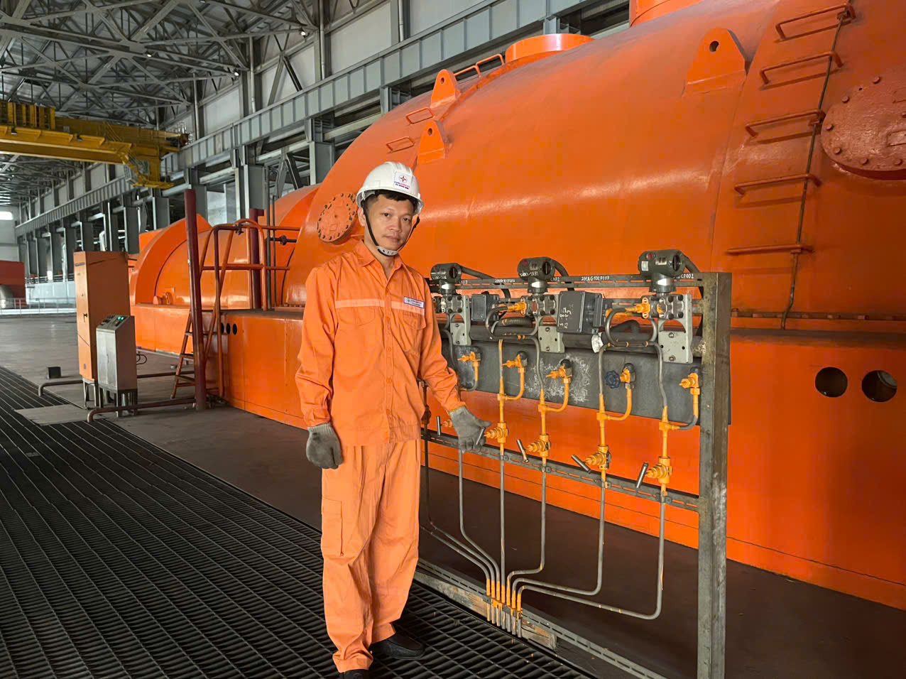 A person in a white helmet standing next to a large orange machineAI-generated content may be incorrect.