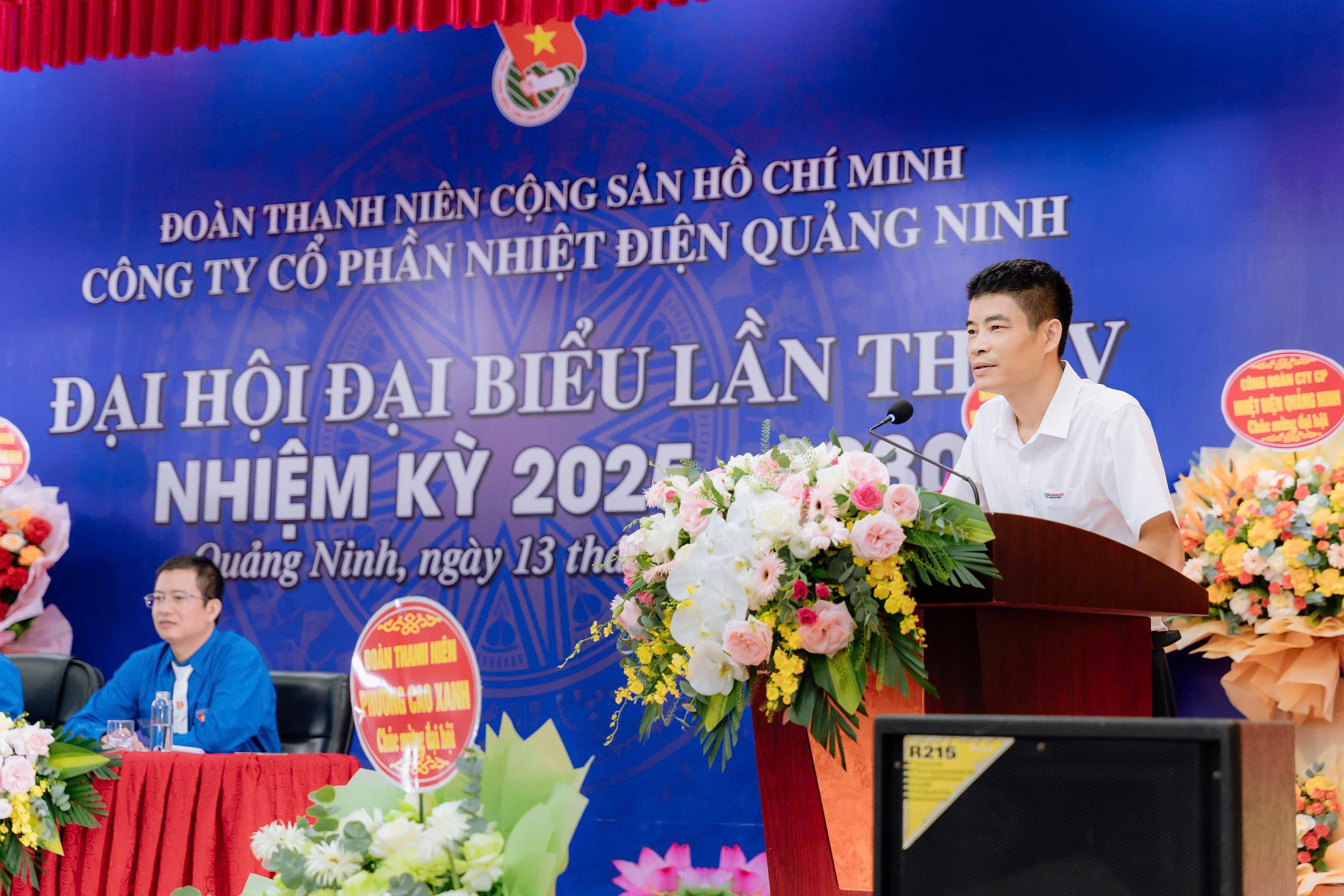 A person standing at a podium with a microphone and flowersAI-generated content may be incorrect.